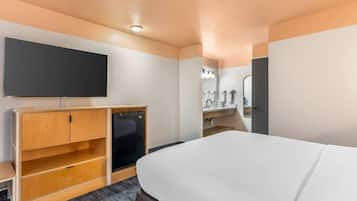 Ein Hotelzimmer mit Bett, Fernseher, Holzschrank und Badezimmer mit Spiegel und Waschbecken.