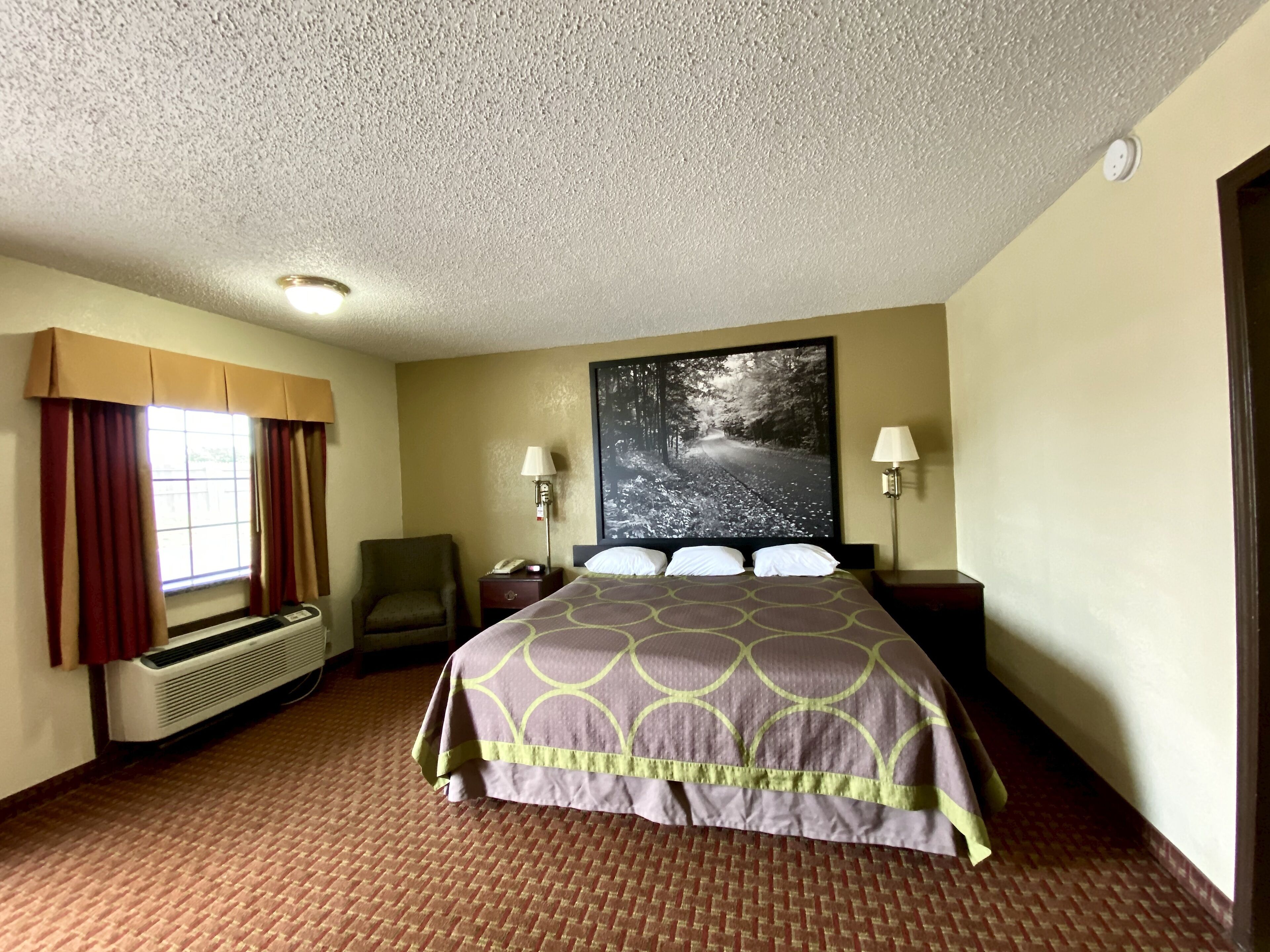 A hotel room with a large bed, a chair, a desk, a lamp, and a window with curtains.