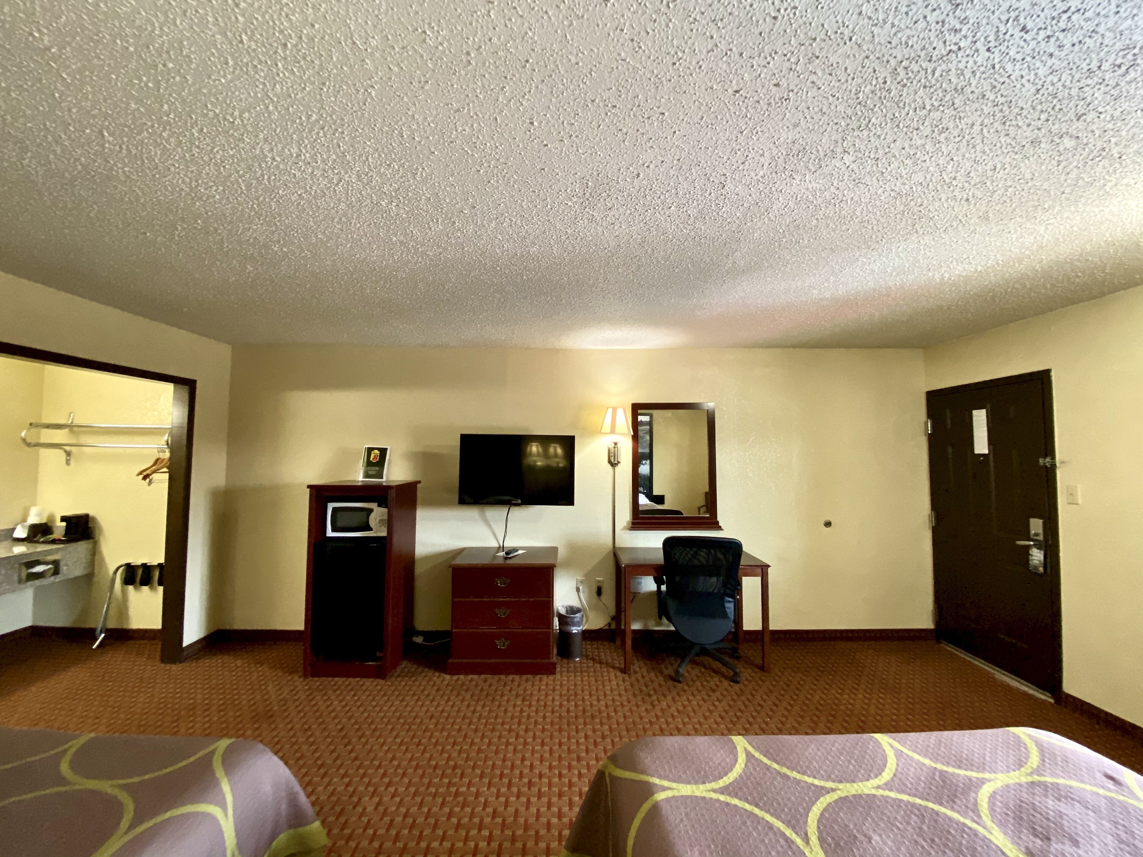 Habitación de hotel con dos camas, un escritorio, una silla, un televisor, un espejo y un microondas.