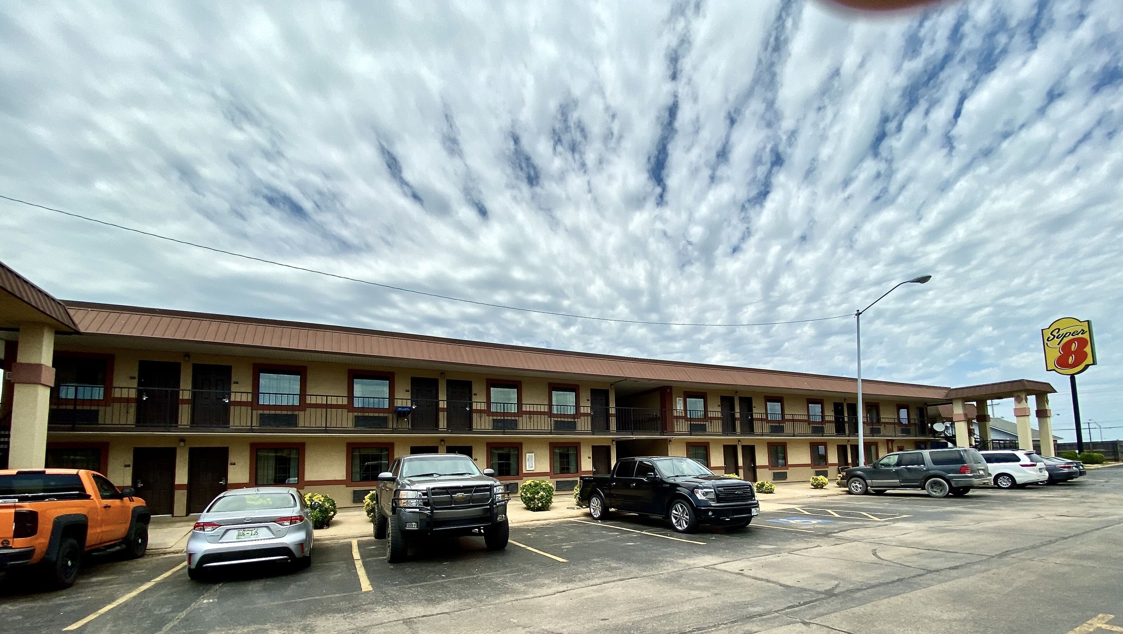 A motel with multiple parking spaces, a large sign indicating 'Super 8', and a clear sky with clouds.