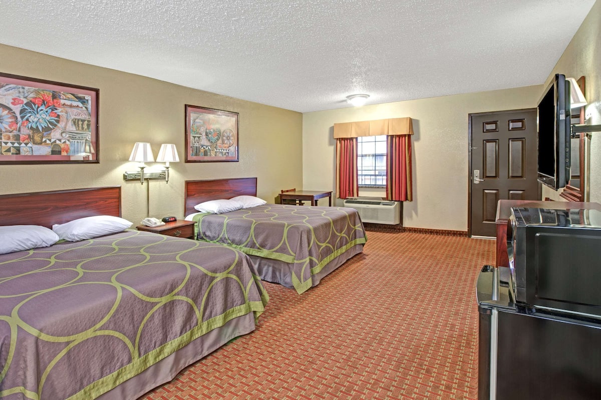 A hotel room with two beds, a desk, a television, and a window with curtains.