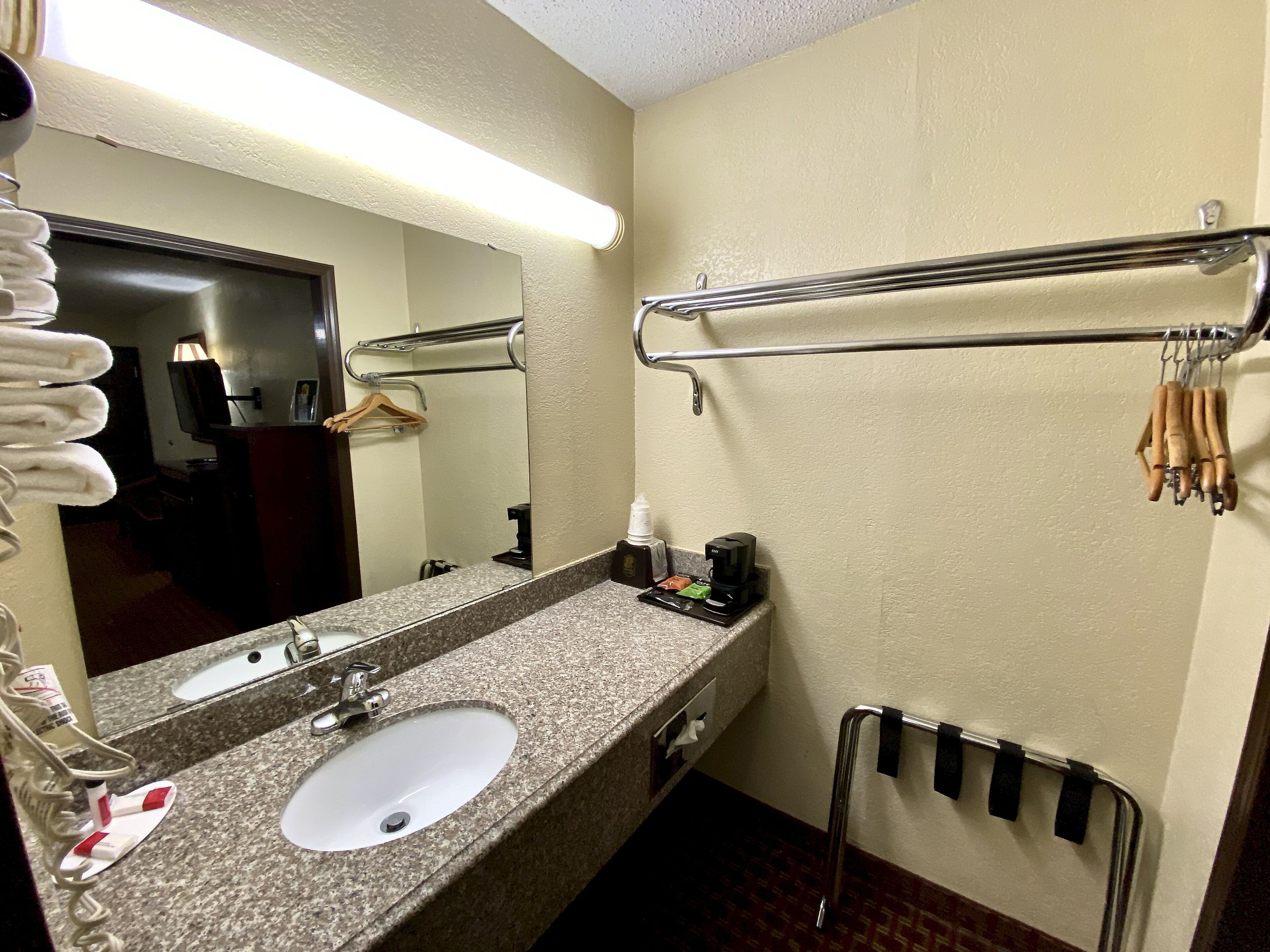 A hotel bathroom with a granite countertop sink, a mirror, a towel rack, and a hand dryer.