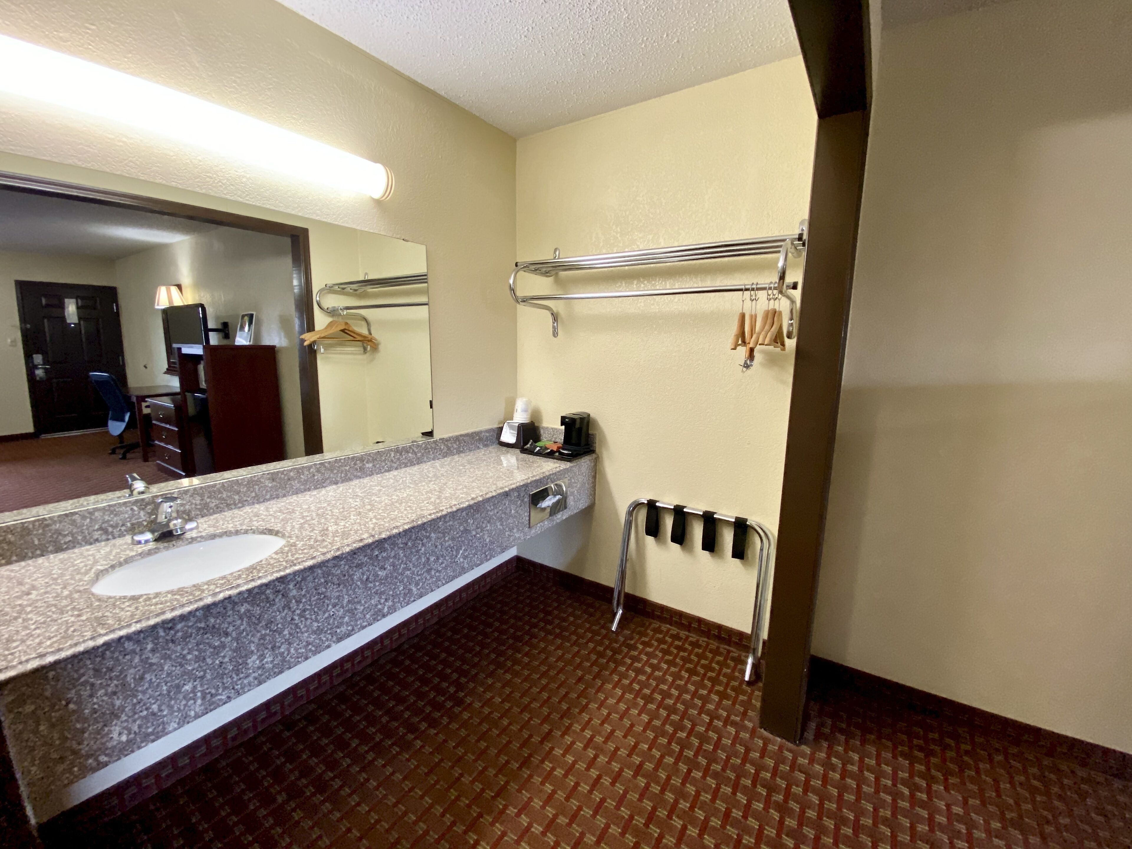 A hotel bathroom with a granite sink, a mirror, a towel rack, and a heated floor.
