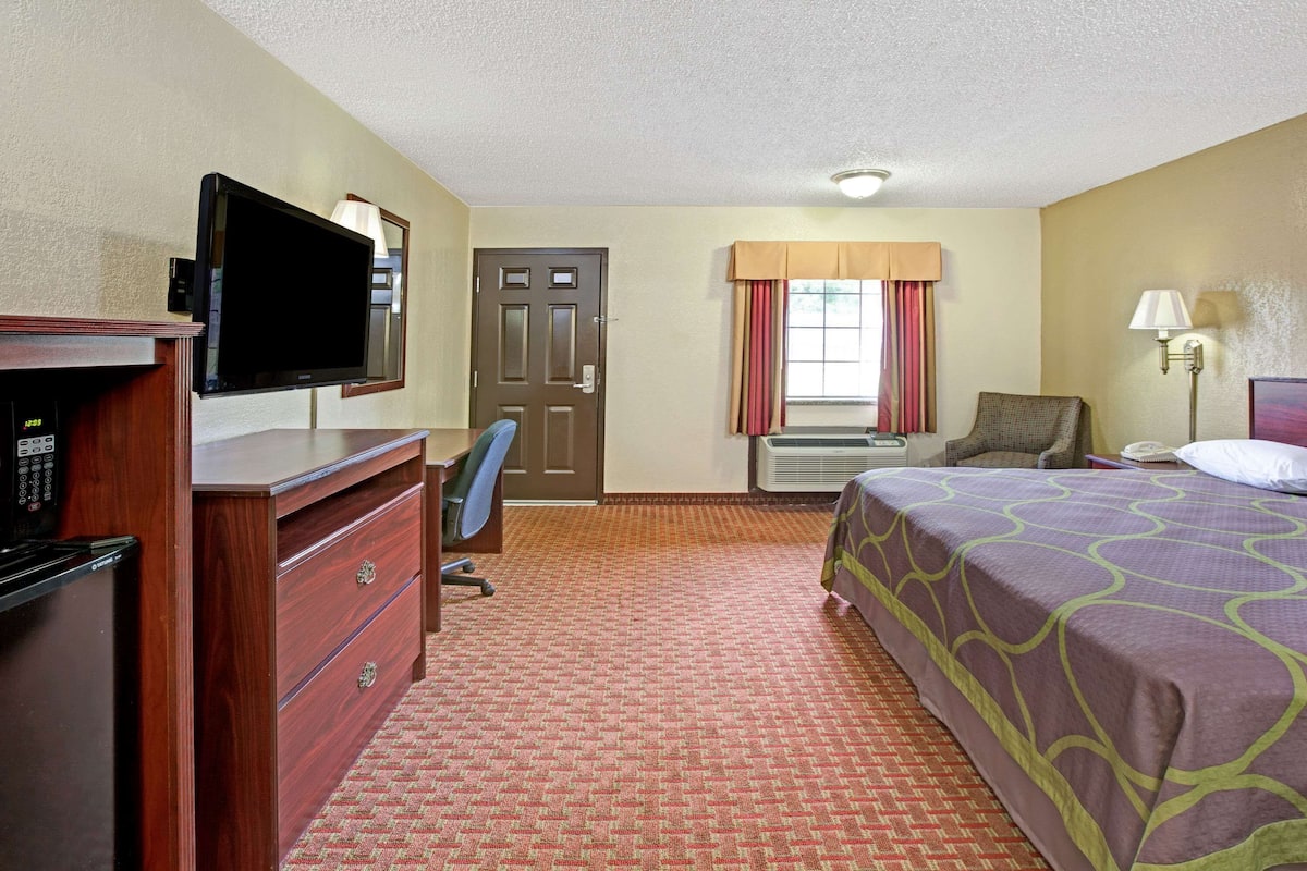 A hotel room with a bed, a desk, a television, a dresser, and an air conditioning unit.
