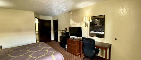 Une chambre d’hôtel avec un lit, un bureau, une chaise, une télévision et un tableau au mur.