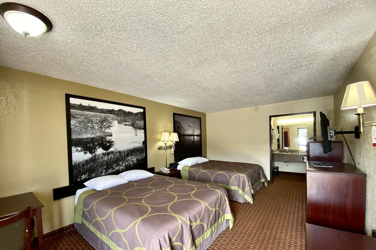 A hotel room with two beds, a desk, a dresser, a mirror, and a large framed picture on the wall.