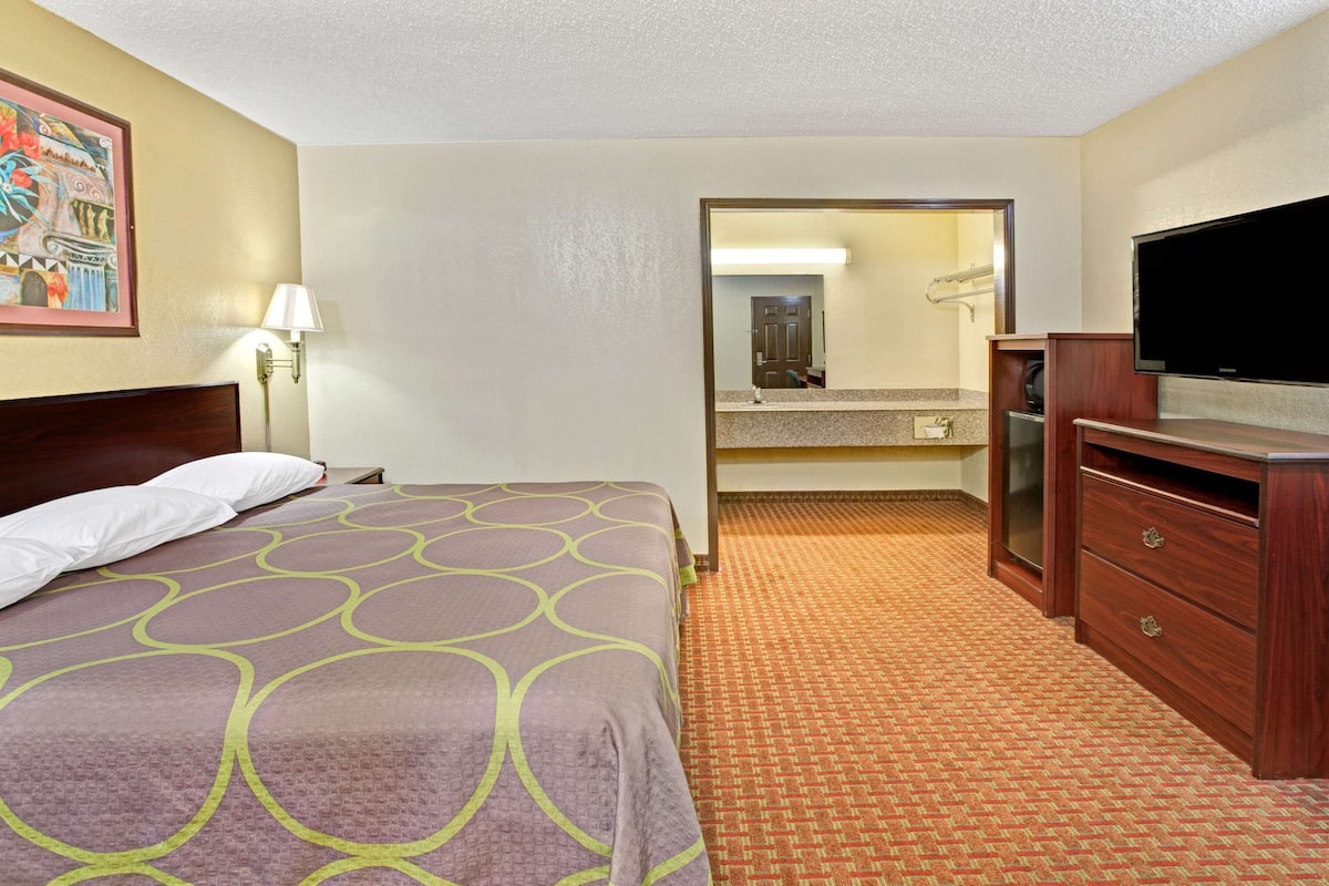 A hotel room with a bed, a television, a dresser, a mirror, and a bathroom visible through an open door.
