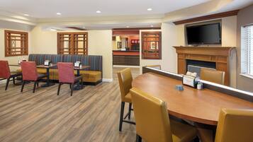 A hotel dining area with a long wooden table, cushioned booths, and red chairs.