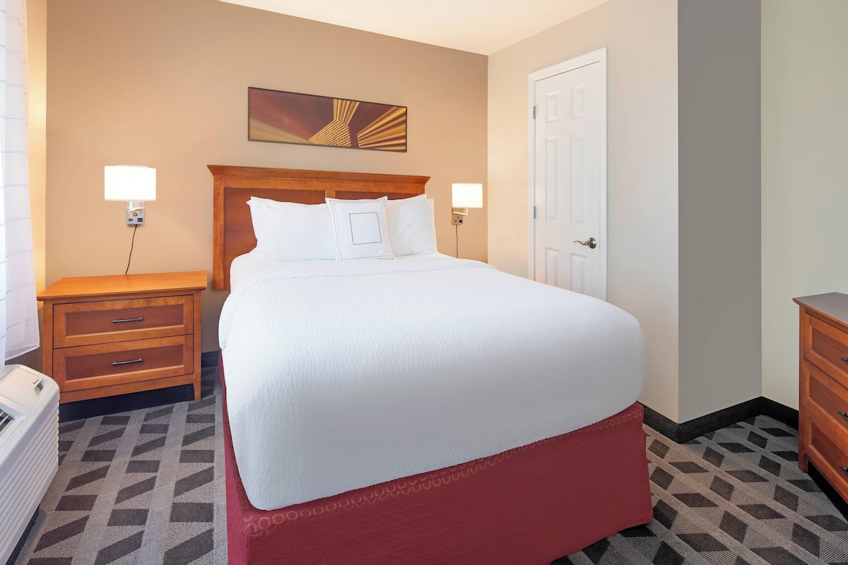 Une chambre d’hôtel avec un grand lit, deux tables de chevet, une œuvre d’art accrochée au mur et une porte.