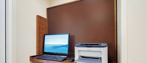 A desk with a laptop, a printer, and a mouse in a corner of a room with a brown partition.