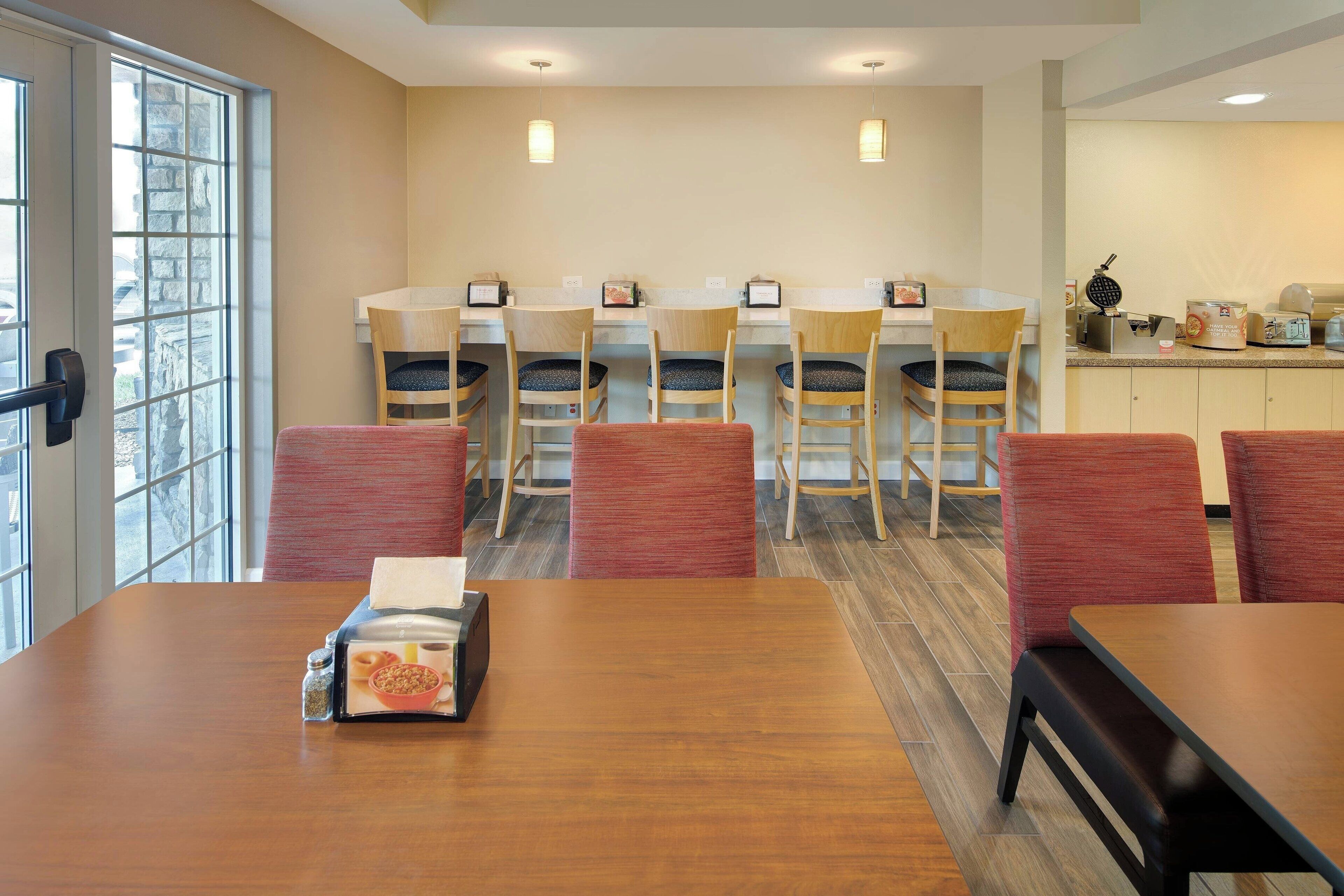 A dining area with a wooden table, red chairs, and a kitchen counter with a waffle maker.