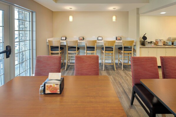 A dining area with a wooden table, red chairs, and a kitchen counter with a waffle maker.