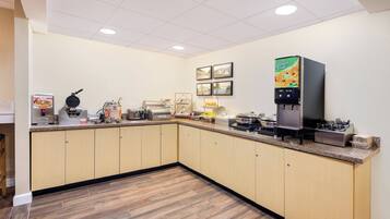 A kitchen with a waffle maker, coffee machine, and a juice dispenser.