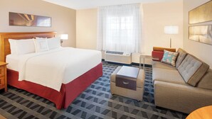 Habitación de hotel con una cama grande, un sofá, una mesita y una ventana con cortinas.