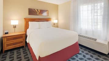 Habitación de hotel con una cama grande, dos mesitas de noche con lámparas, una obra de arte en la pared, una ventana con cortinas traslúcidas y una alfombra estampada.