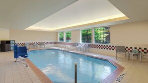 Una piscina con plataforma de baldosas, un trampolín y sillas alrededor.
