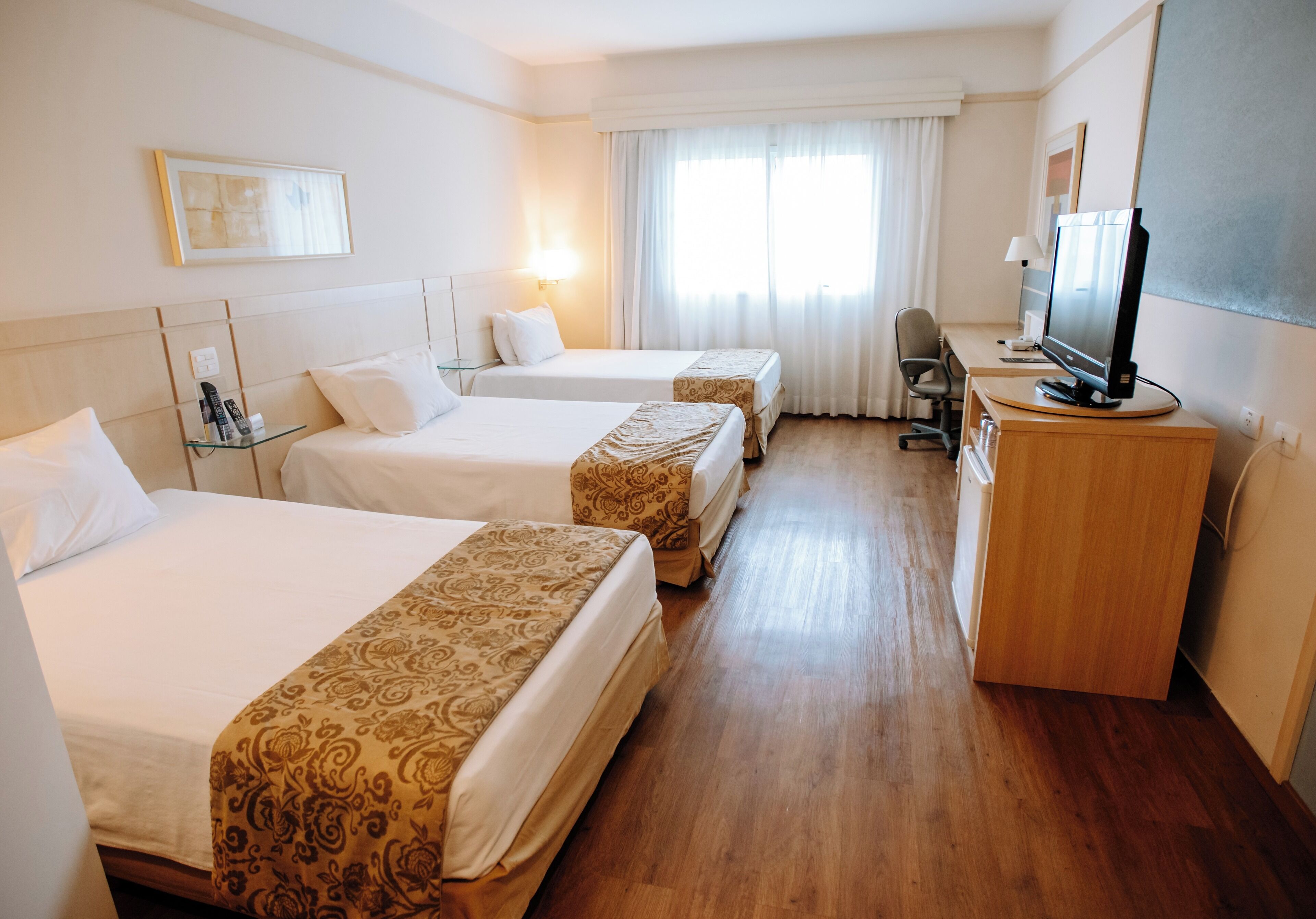 A hotel room with two beds, a desk with a computer, a chair, and a television.