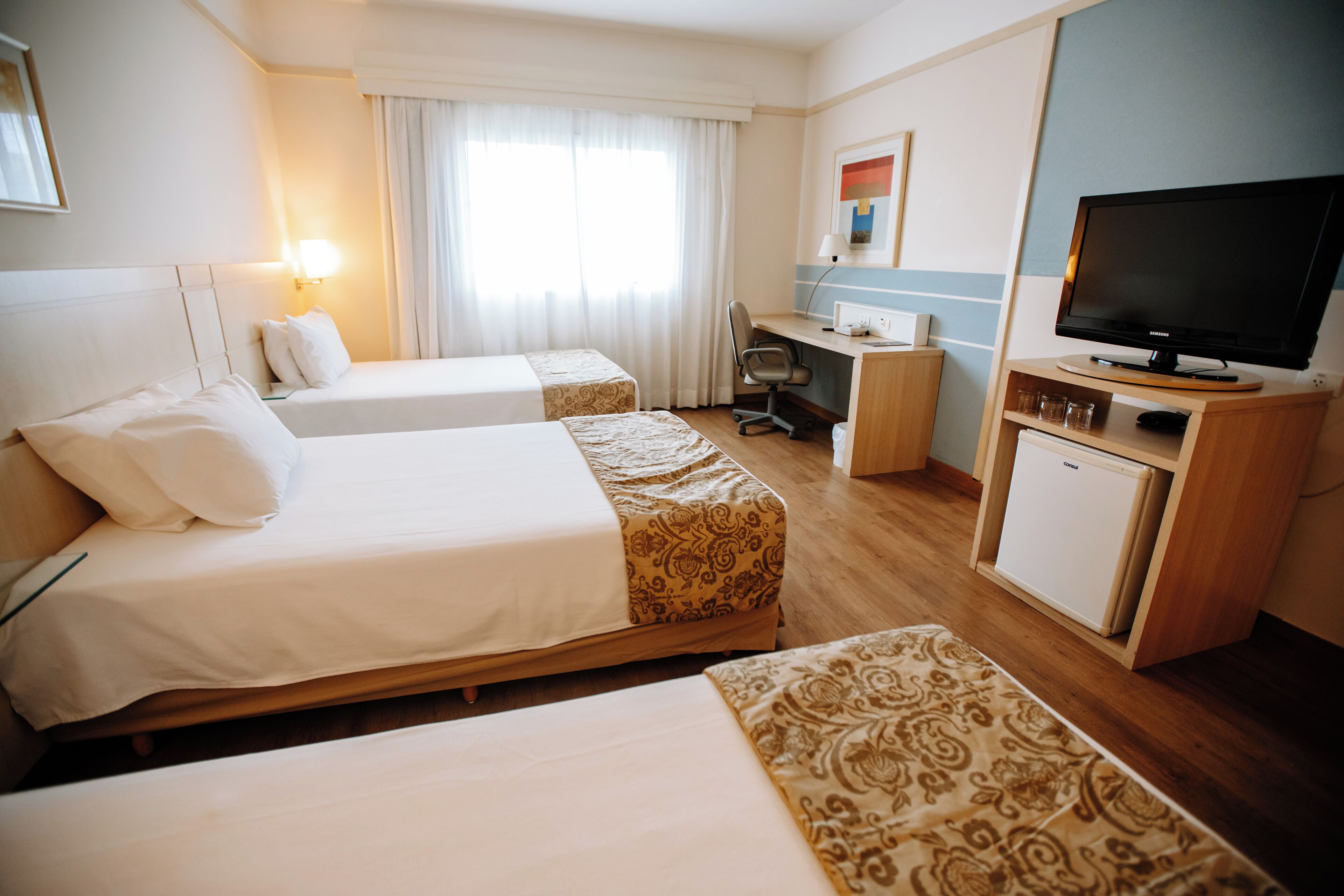 A hotel room with two beds, a desk, a television, and a mini-fridge.