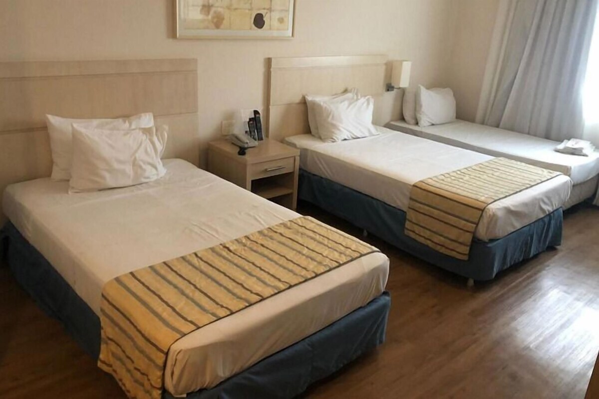 A hotel room with two beds, a nightstand, a lamp, and a painting on the wall.