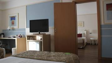 A hotel room with a bed, a desk with a television, a small refrigerator, and a door leading to another room.