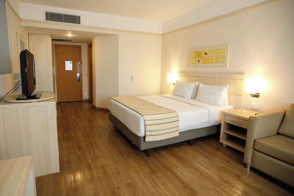 A hotel room with a bed, bedside tables, a TV, and a door leading to another room.