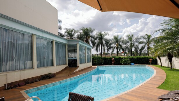 Une piscine avec une terrasse en bois, un patio couvert et une vue sur les palmiers.