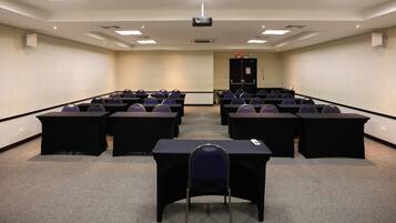 A conference room with rows of tables and chairs, a projector, and a door in the background.