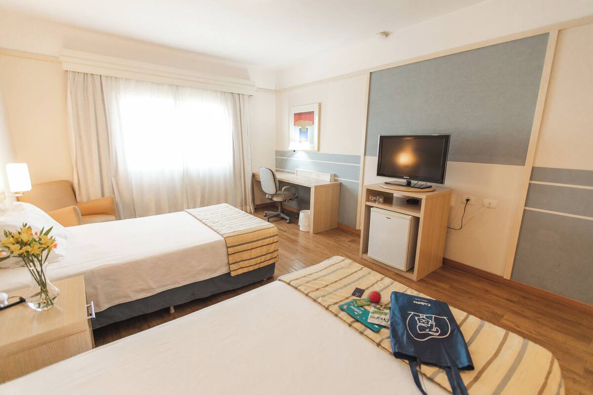 A hotel room with two beds, a desk, a television, and a small kitchenette.