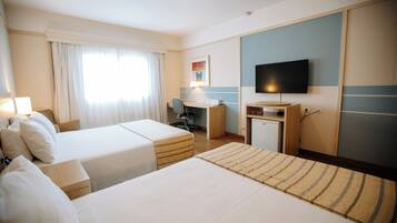 Quarto de hotel com duas camas, uma escrivaninha, televisão e uma pequena cozinha.