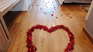 Une chambre d’hôtel avec un chemin de pétales de rose en forme de cœur menant au lit.