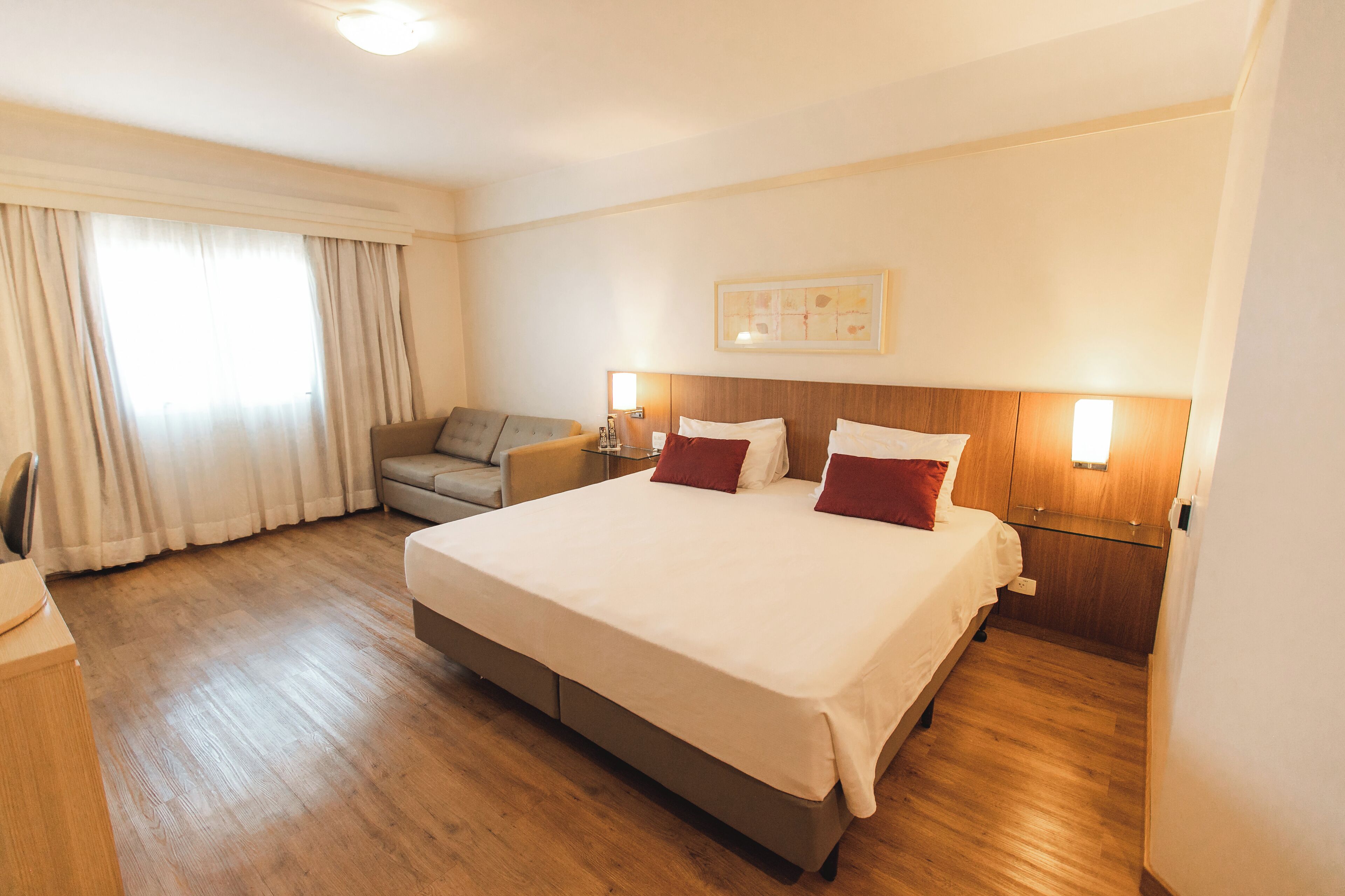 Quarto de hotel com uma cama grande, um sofá, uma mesa e uma janela com cortinas.