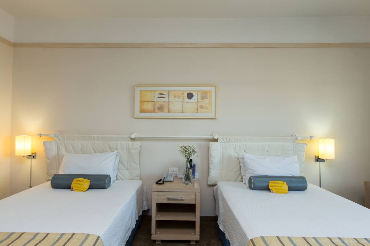 Una habitación de hotel con dos camas, una mesita de noche, una lámpara y un cuadro en la pared.