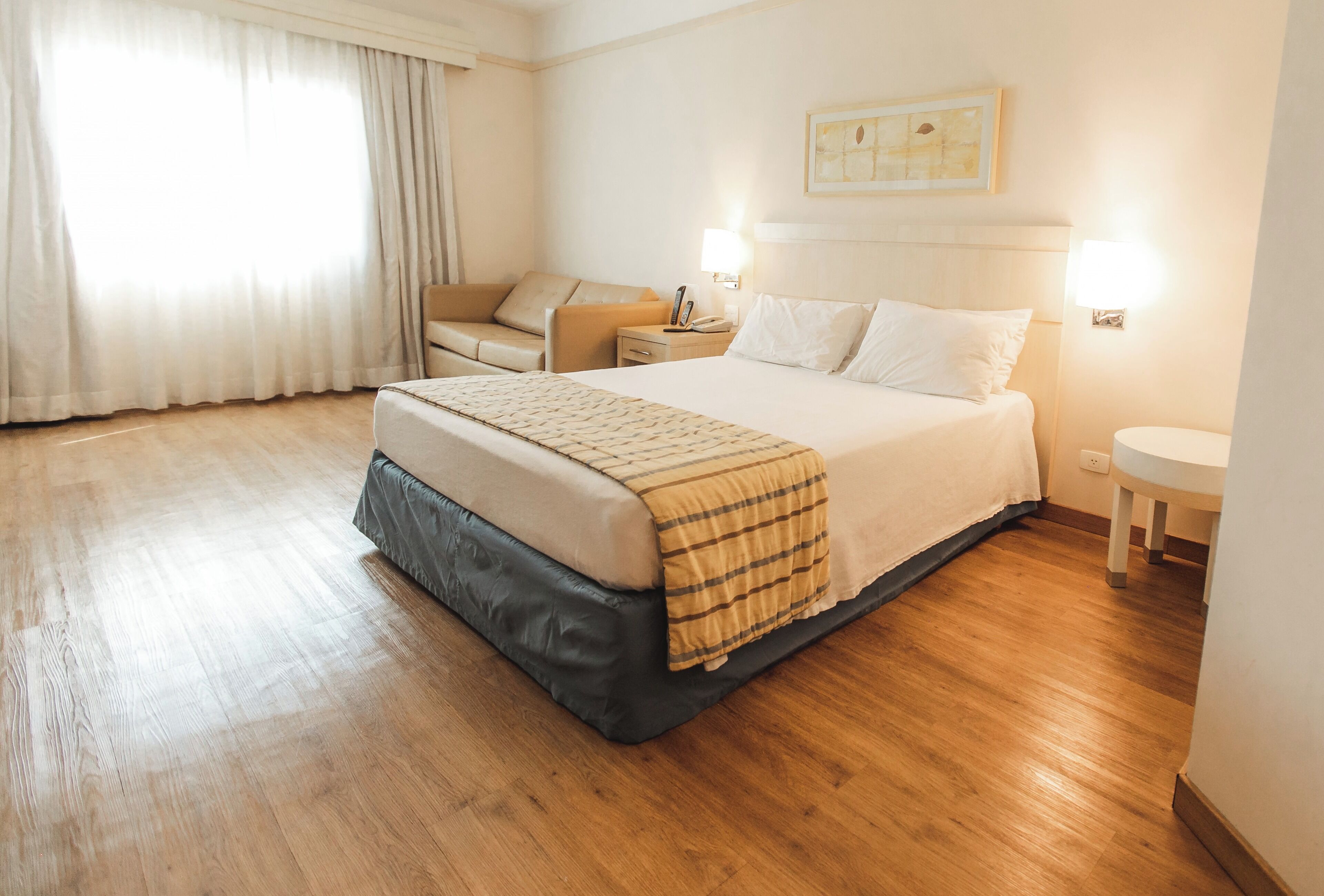 Habitación de hotel con una cama grande, una mesita de noche, una lámpara y una ventana con cortinas.