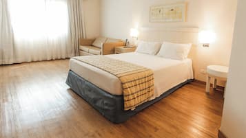 Habitación de hotel con una cama grande, una mesita de noche, una lámpara y una ventana con cortinas.