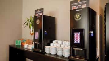 Una estación de café con dos máquinas de café y pilas de tazas blancas.
