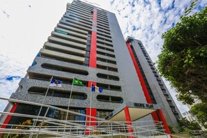 A tall building with multiple floors, a prominent red stripe, and several flags. - Garvey Inn Recife Flat (Recife)
