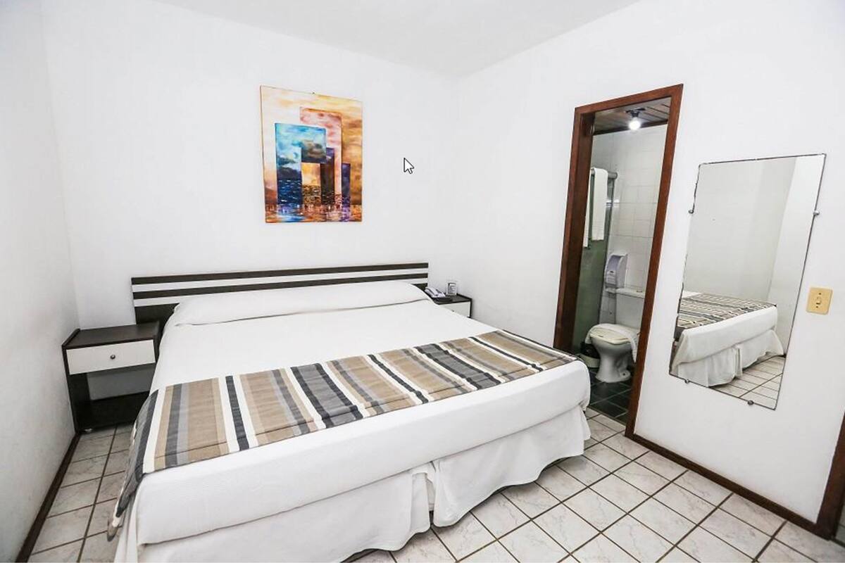 A hotel room with a bed, a nightstand, a bathroom with a toilet, and a mirror.