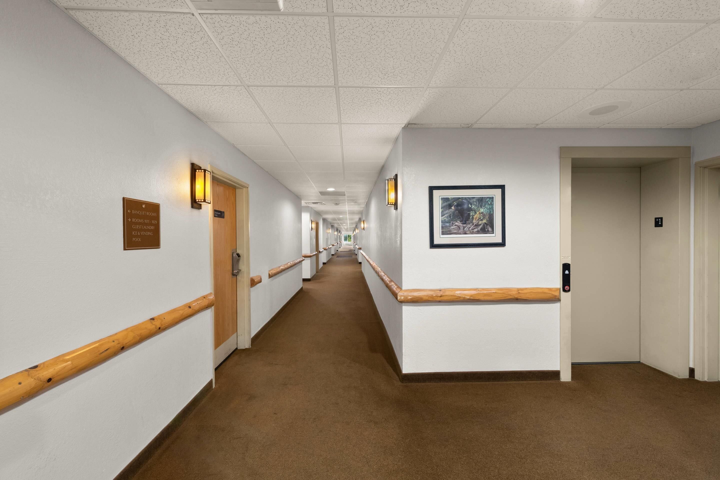 A hotel corridor with doors, a framed picture, and a sign indicating amenities like banquet rooms and a pool.