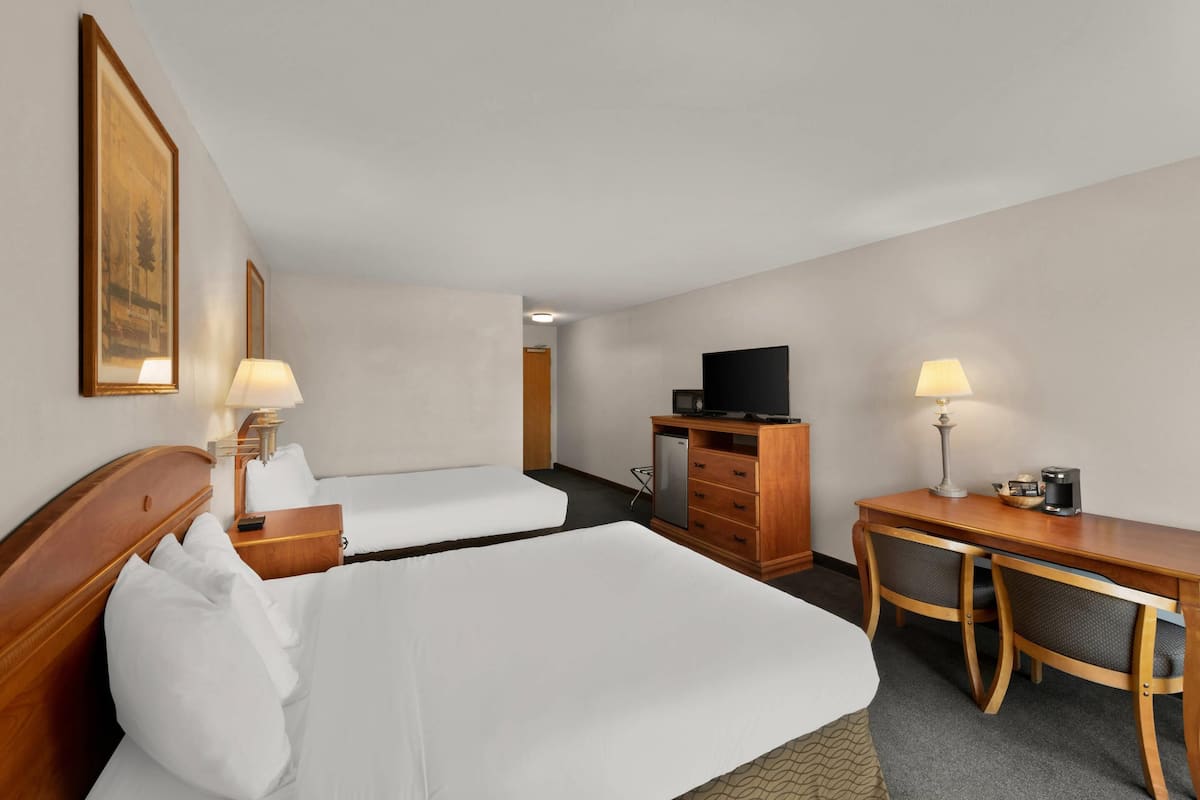 A hotel room with two beds, a desk, a chair, a TV, and a coffee maker.