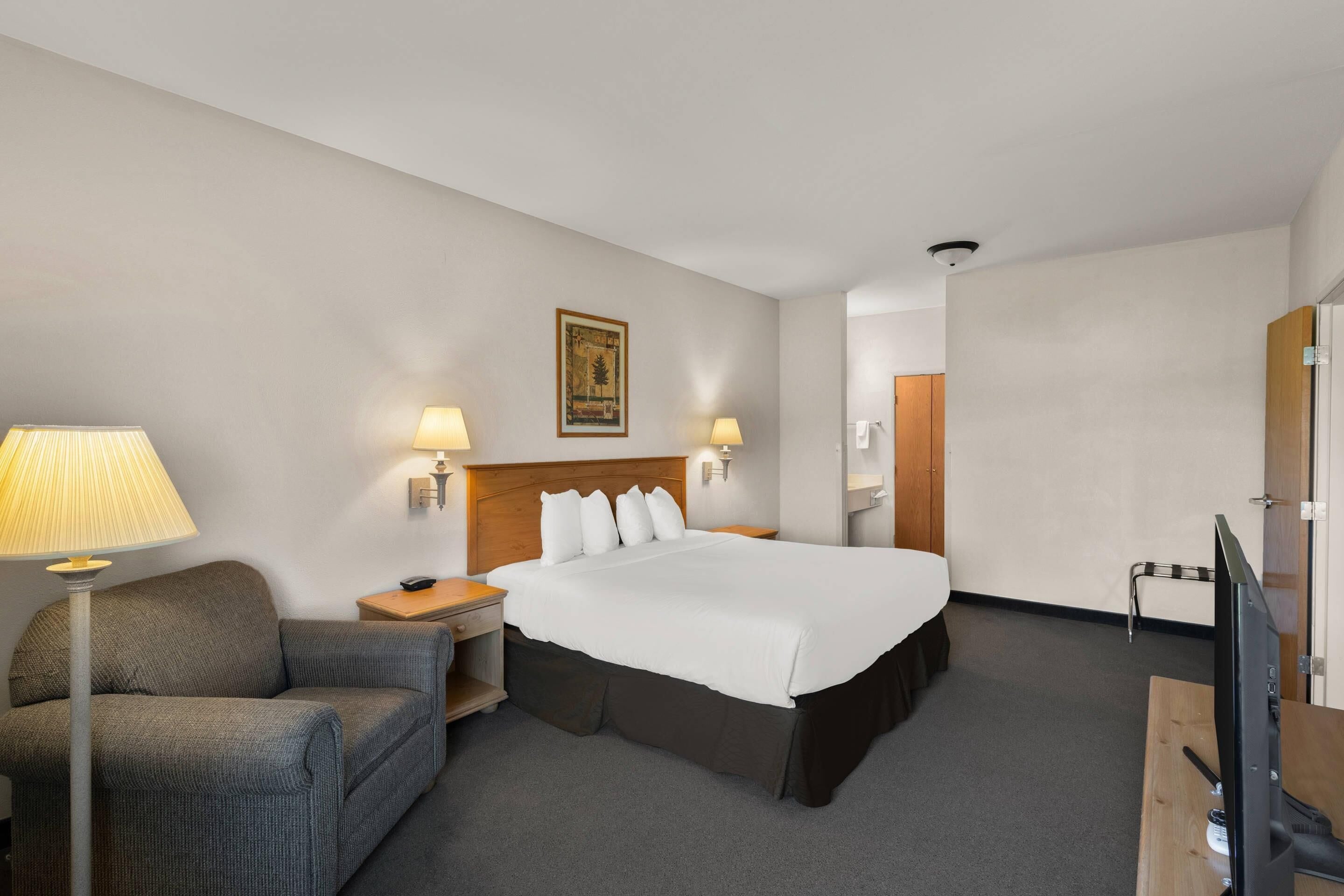 A hotel room with a bed, two bedside lamps, a desk with a computer, a chair, and a television.