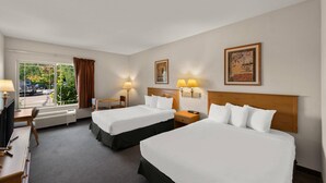 Una habitación de hotel con dos camas, un escritorio, una silla, un televisor y una ventana con cortinas.