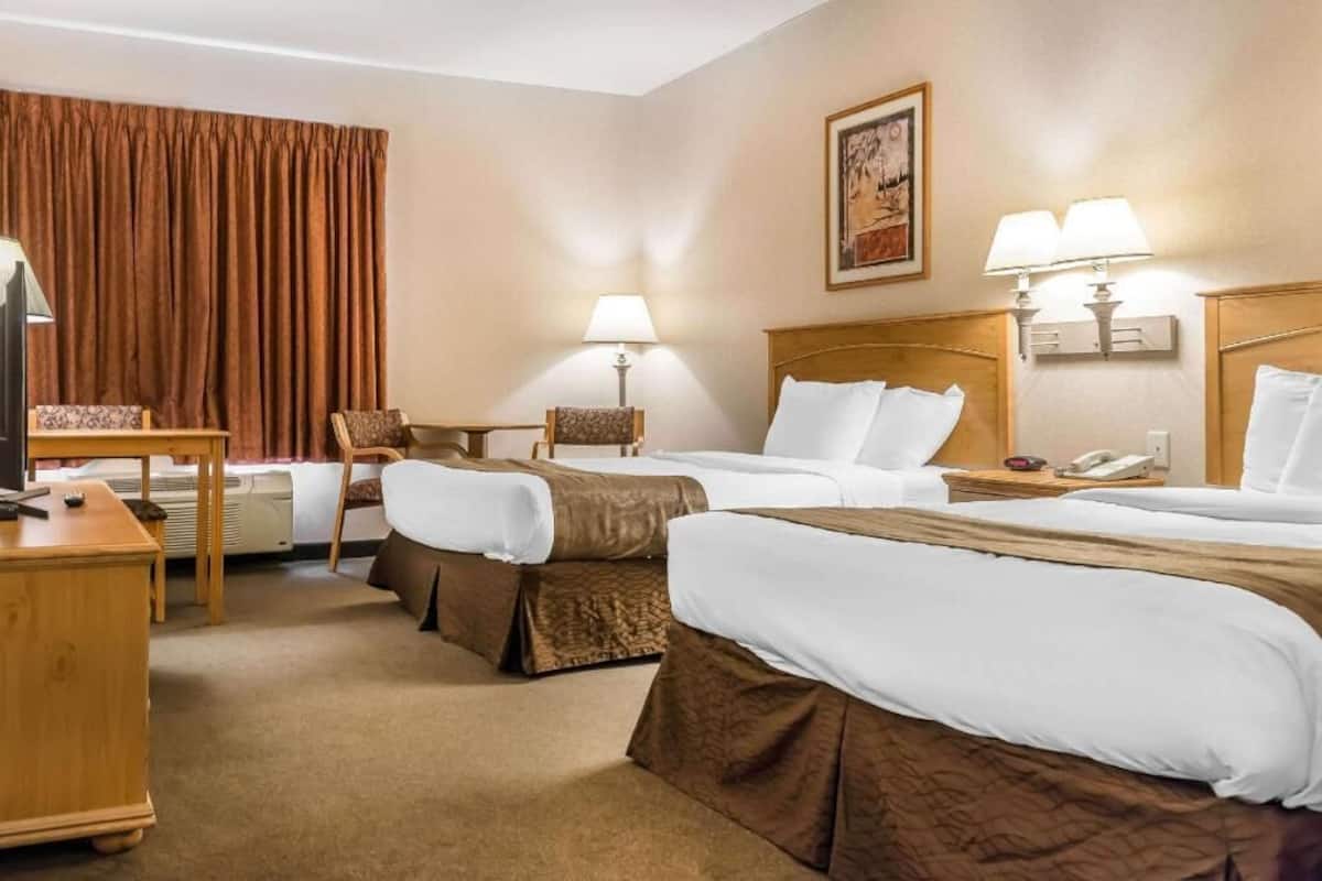 A hotel room with two beds, a desk, a chair, a television, and two lamps.