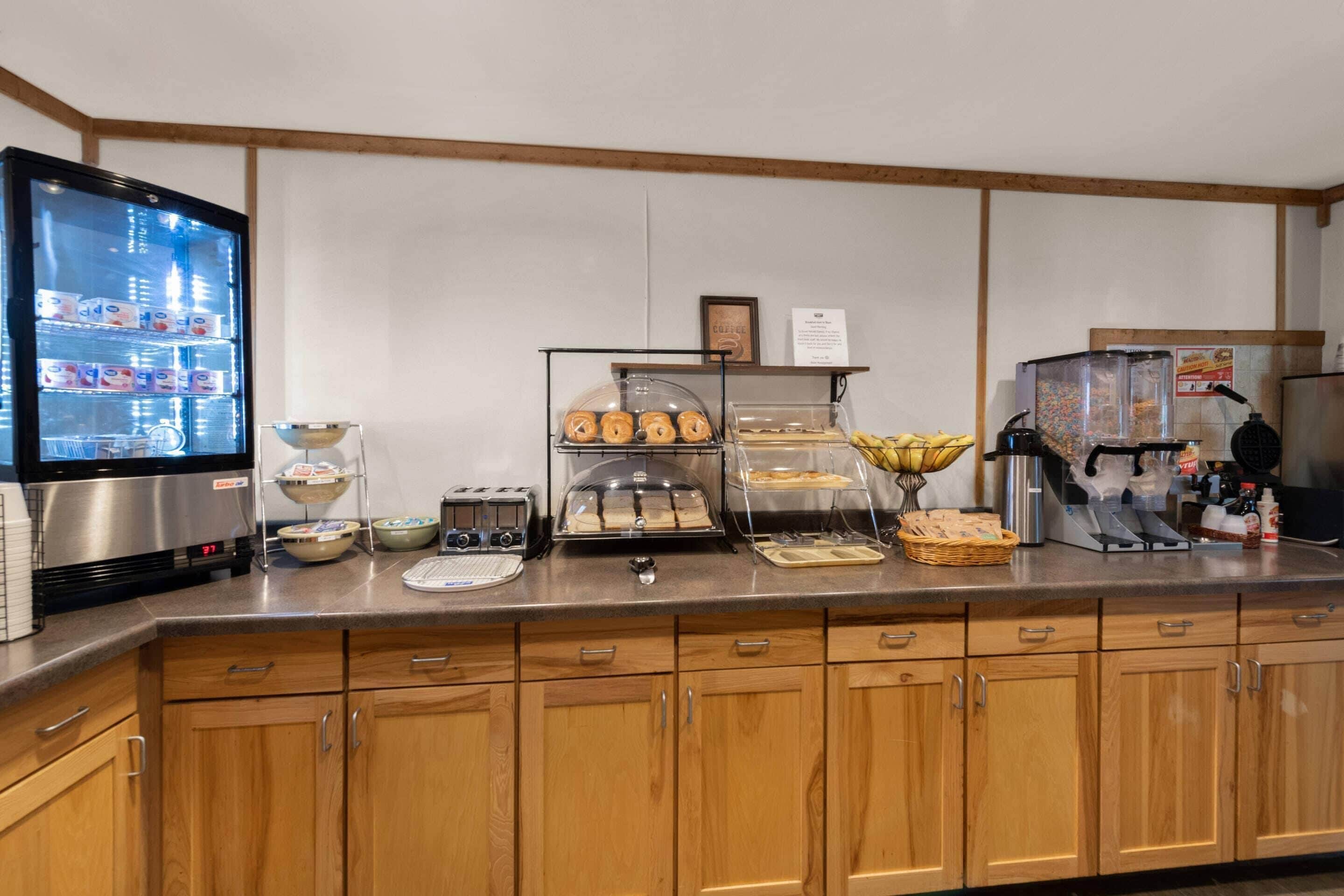 A self-service breakfast area with a refrigerator, toaster, and various food items.
