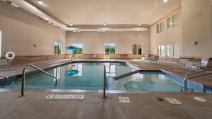 Piscina interior con señalización clara, sillas de descanso y vistas al exterior.