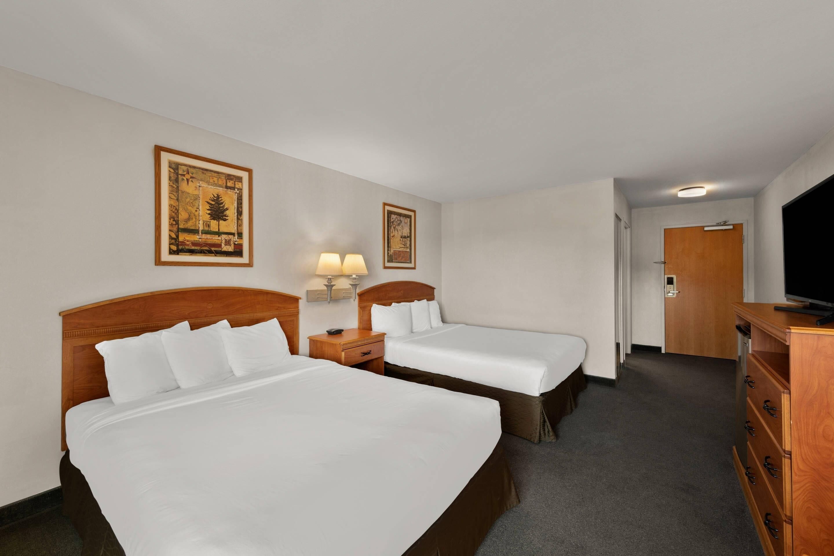 A hotel room with two beds, a wooden dresser, a television, and framed artwork on the walls.
