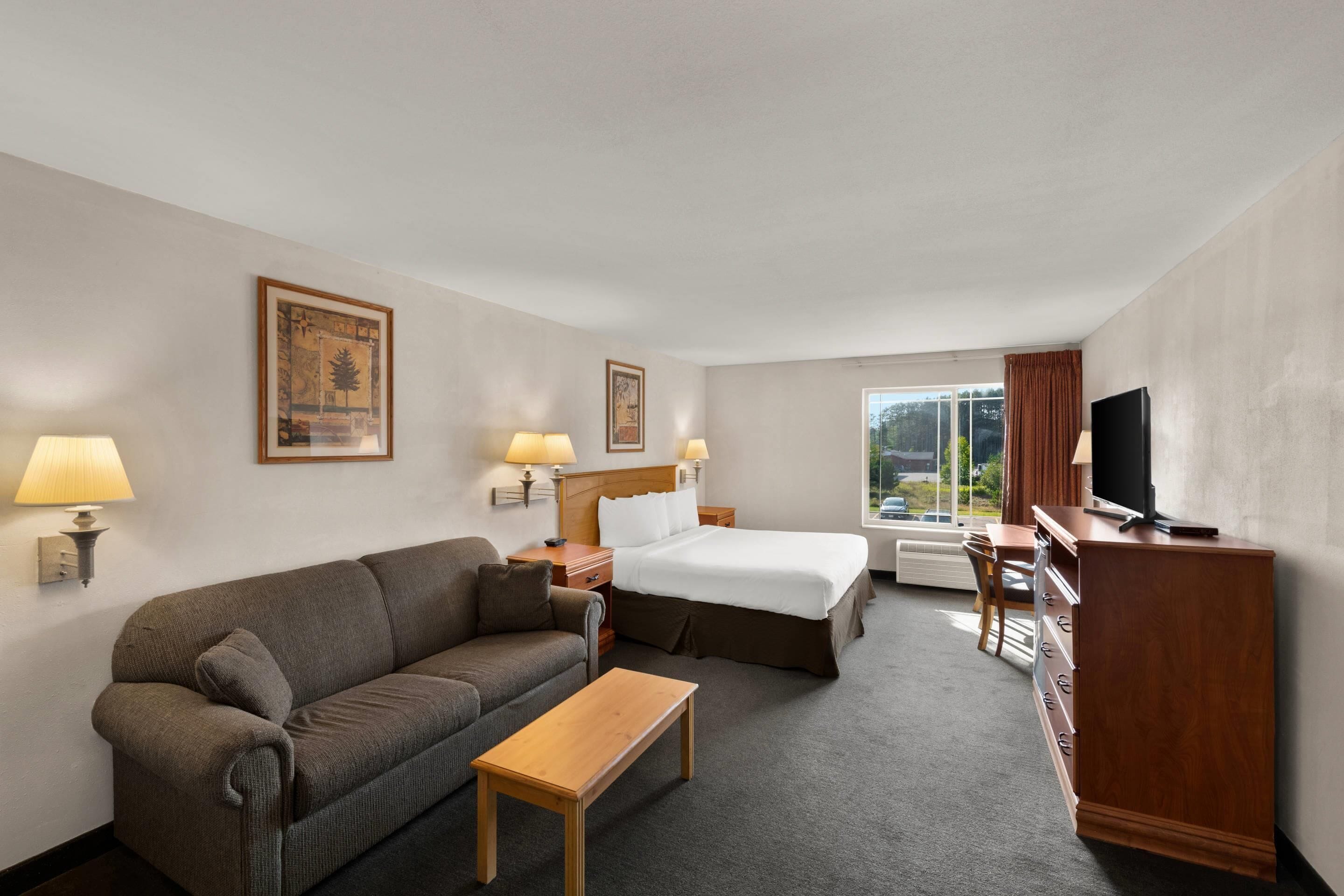Habitación de hotel con cama, sofá, escritorio, televisor y ventana con cortinas.