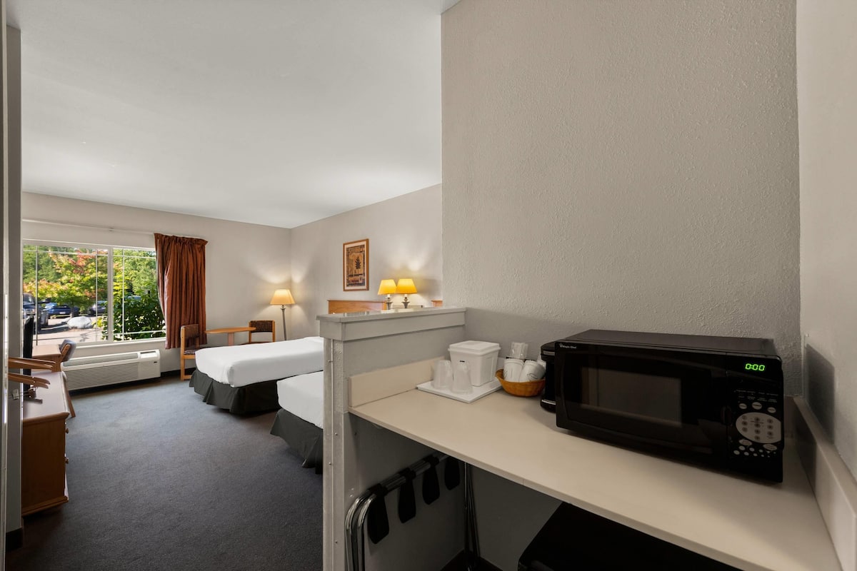 A hotel room with a bed, a desk, a microwave, a coffee maker, and a window with curtains.