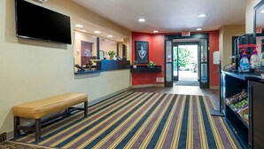 Un hall d’hôtel avec un comptoir d’accueil, un banc, un téléviseur et un panneau indiquant la sortie.