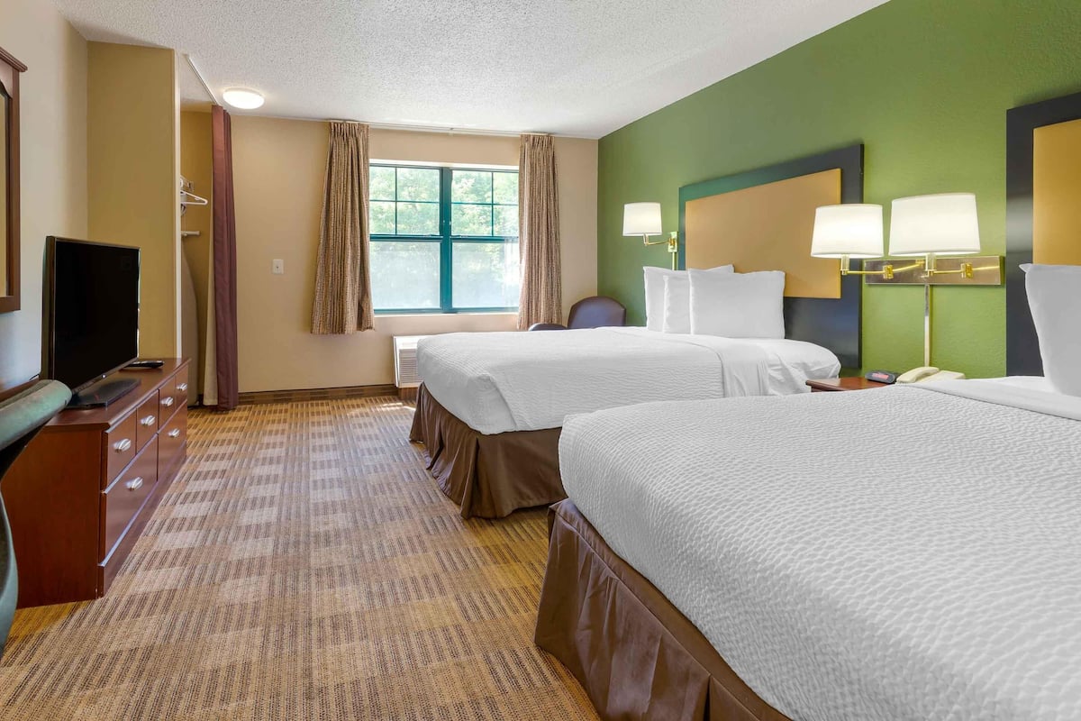 Une chambre d’hôtel avec deux lits, un bureau avec une télévision et une fenêtre avec des rideaux.