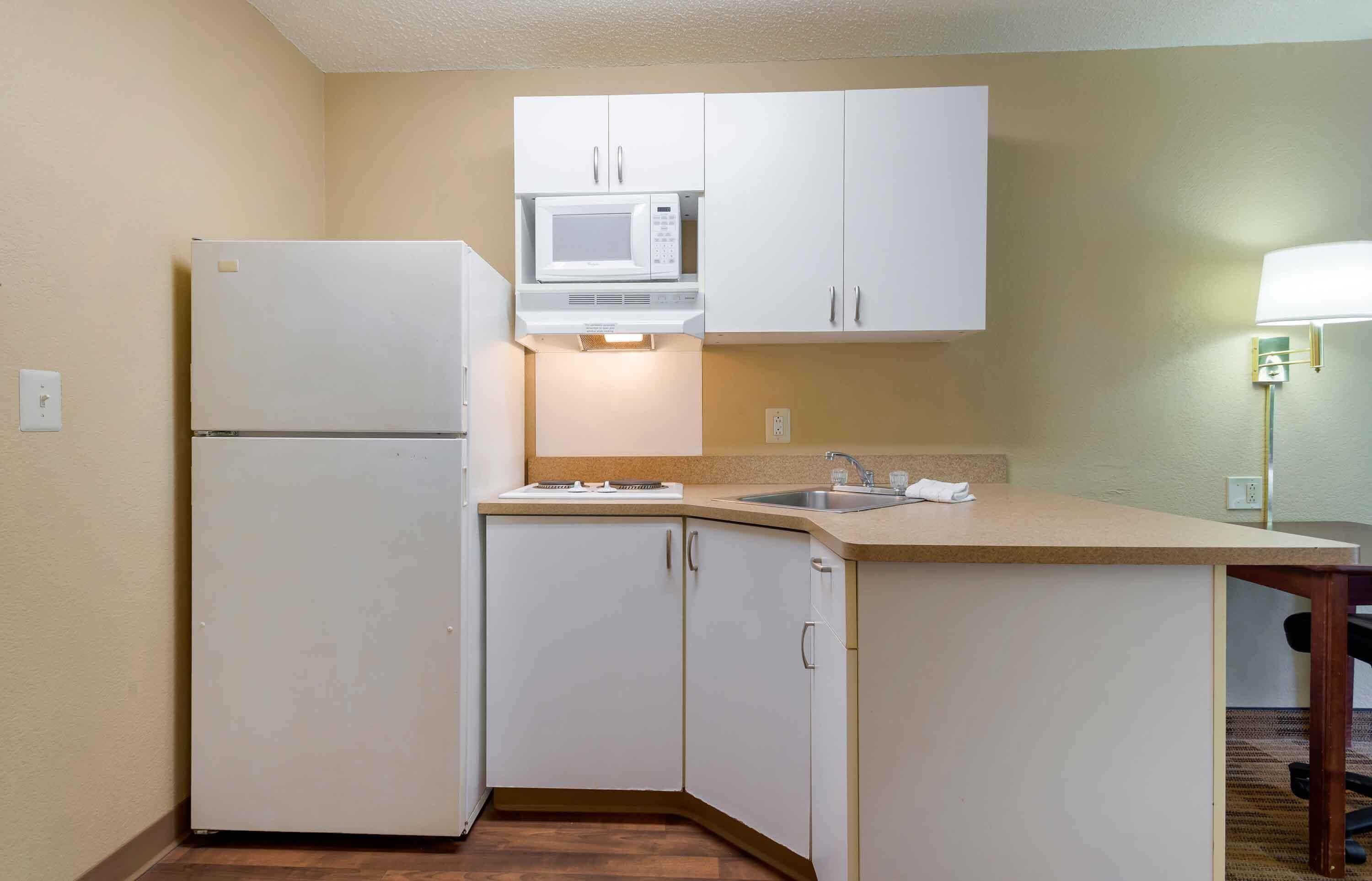 A compact kitchen with white cabinets, a microwave, a refrigerator, and a sink.